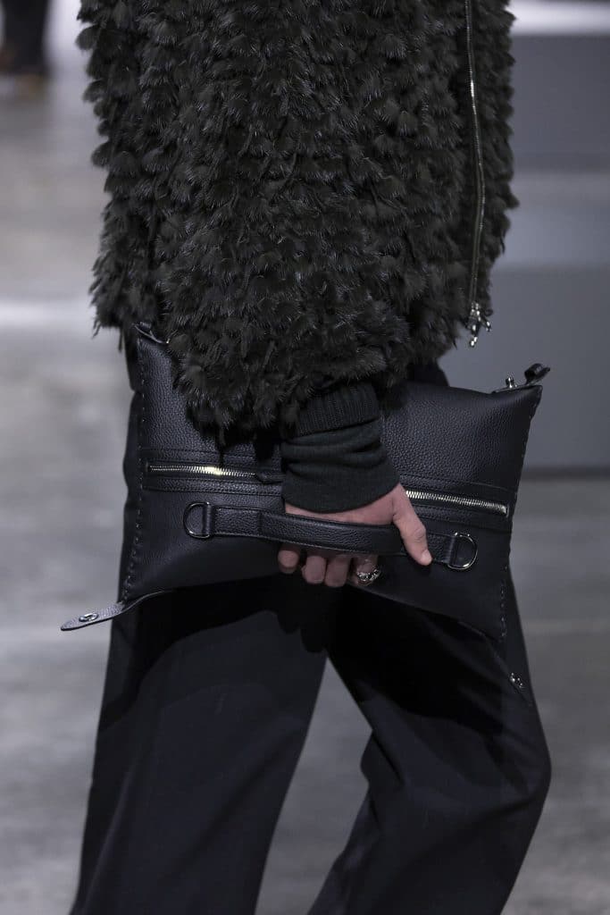 Người đàn ông mặc áo khoác lông và quần đen cầm túi xách da màu đen