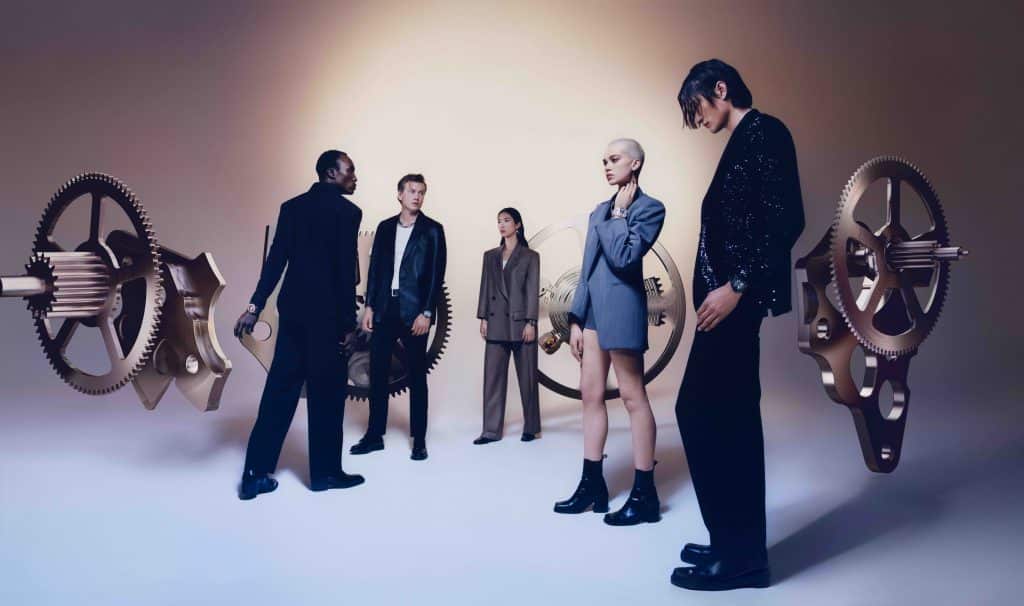 Năm người mẫu mặc trang phục lịch sự tạo dáng cùng các bánh răng đồng hồ lớn