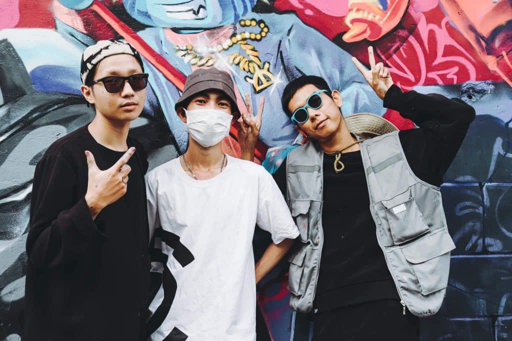 Ba bạn trẻ tạo dáng trước bức tường graffiti đầy màu sắc