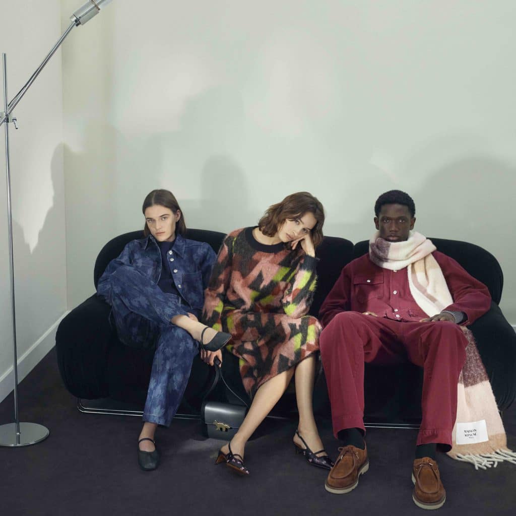 Ba người mẫu mặc trang phục thu đông Maison Kitsune ngồi trên ghế sofa màu đen