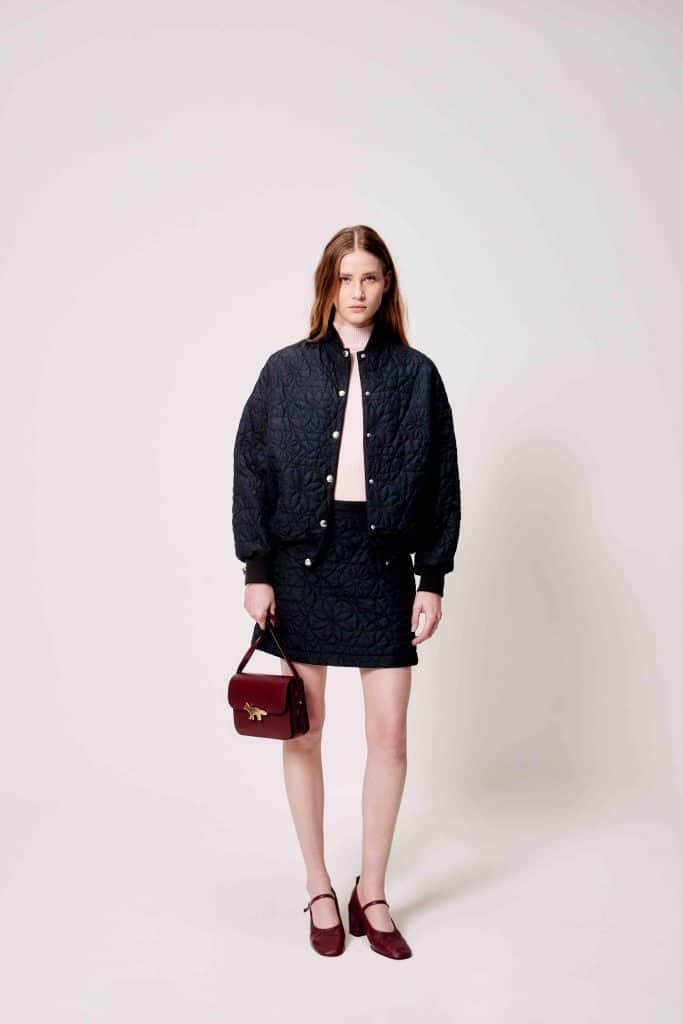 Người mẫu mặc áo khoác và váy đen cùng túi xách màu đỏ burgundy