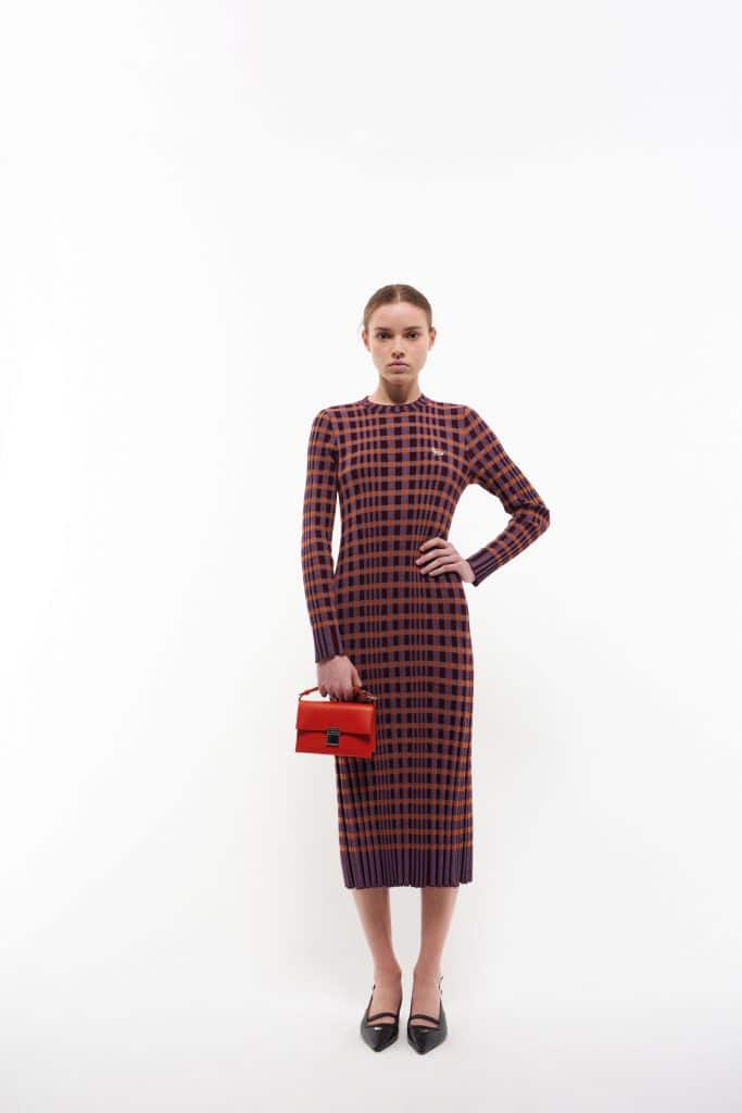 Người mẫu mặc váy len kẻ caro màu cam và cầm túi xách đỏ trên nền trắng