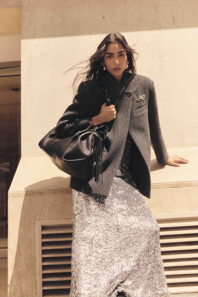 Người mẫu mặc áo blazer và váy lấp lánh cầm túi xách đen tạo dáng bên ngoài tòa nhà