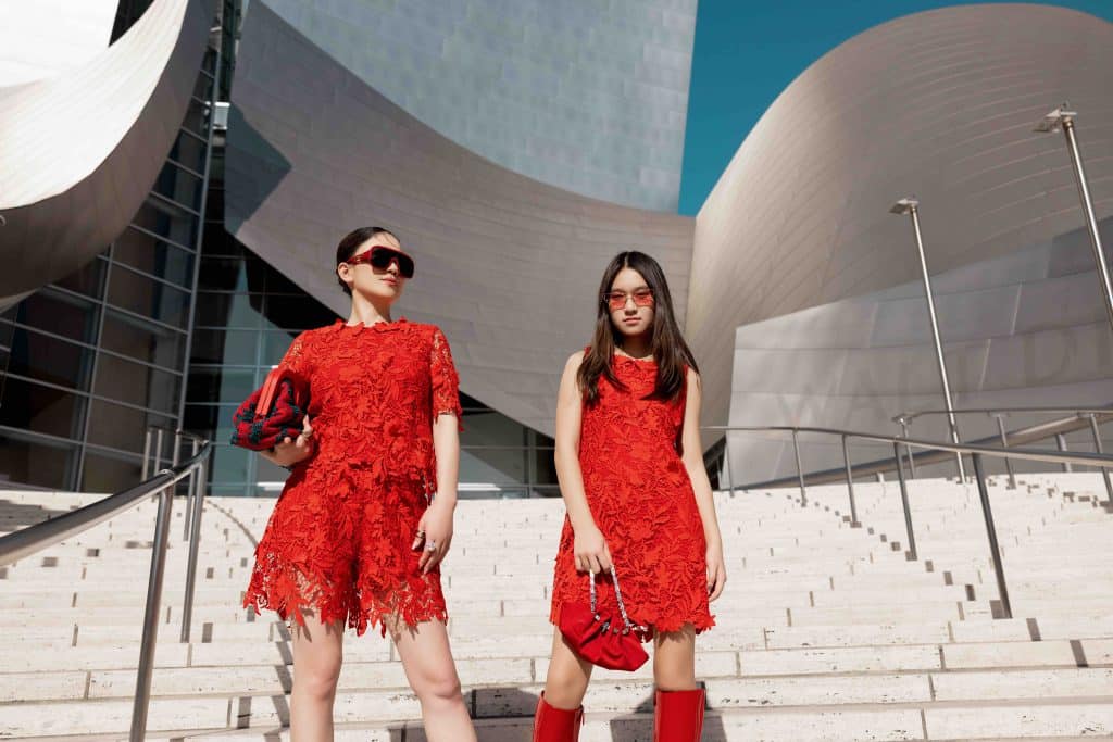 Mẹ và con gái diện đồ đôi màu đỏ tươi tắn trước tòa nhà hiện đại