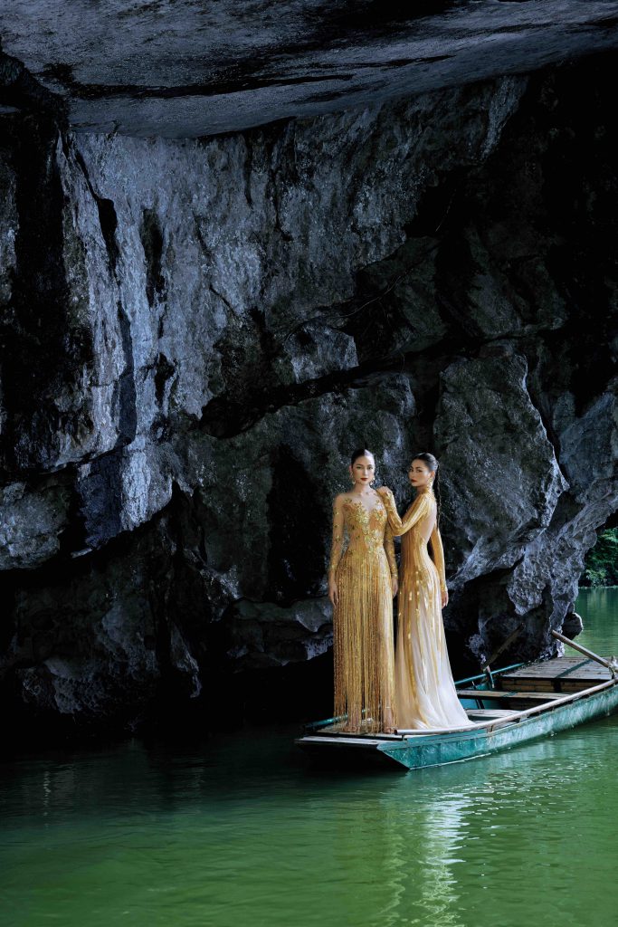 Hai người mẫu mặc áo dài vàng trên thuyền nhỏ trong hang động xanh biếc