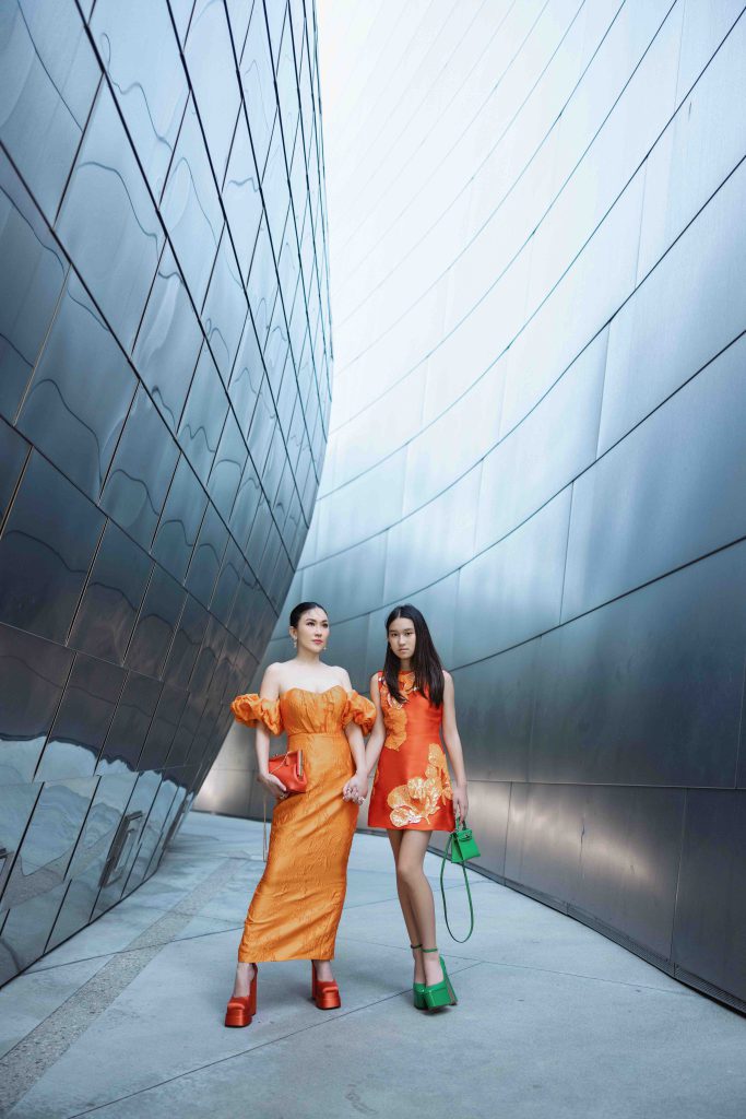 Mẹ và con gái diện đồ đôi màu cam nổi bật trước tòa nhà kiến trúc hiện đại