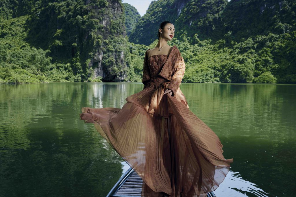 Người mẫu mặc váy dài duyên dáng trên thuyền giữa phong cảnh núi non xanh biếc