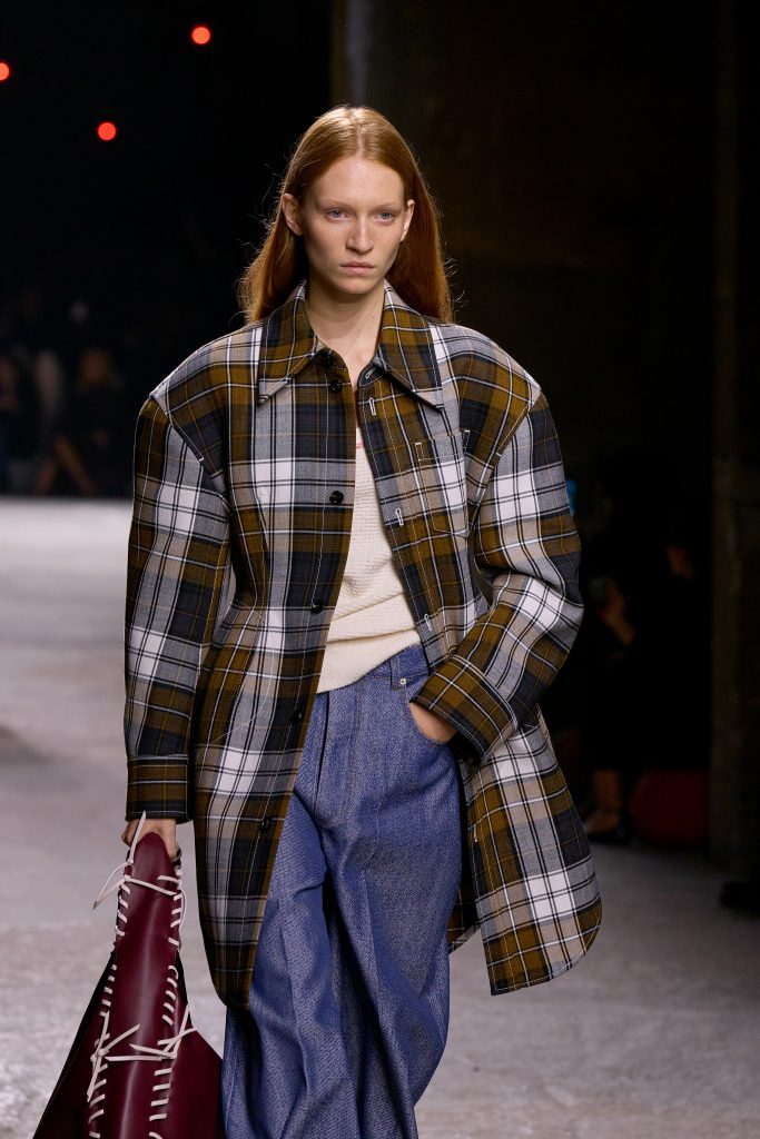 Người mẫu trình diễn áo khoác kẻ caro dáng rộng và quần jean trên sàn catwalk