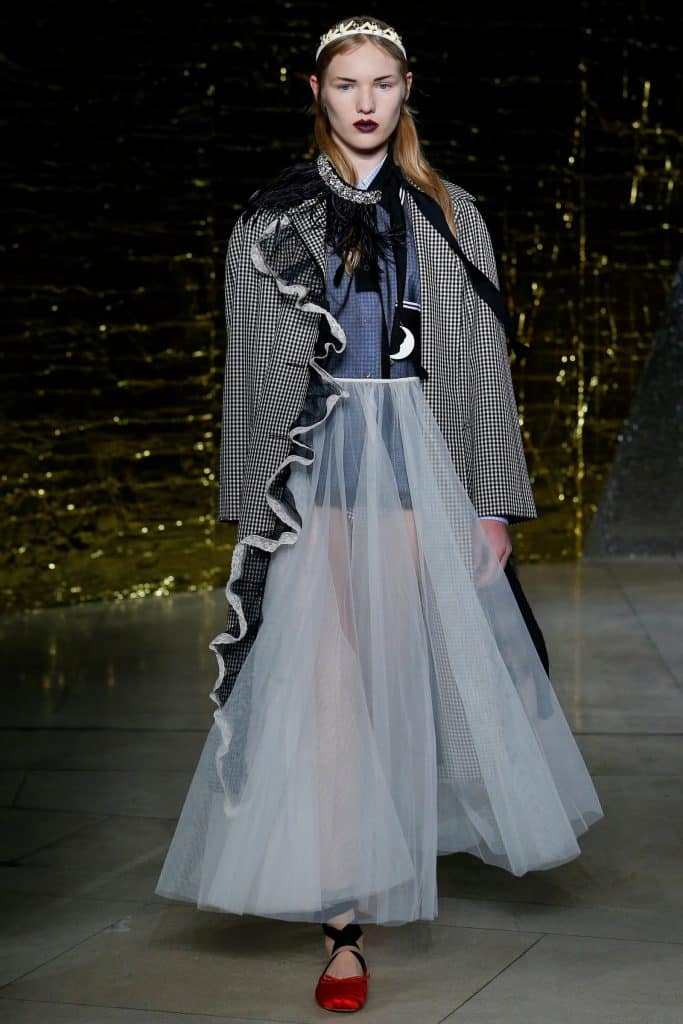 A model walks the runway wearing a checkered coat and a flowing tulle skirt