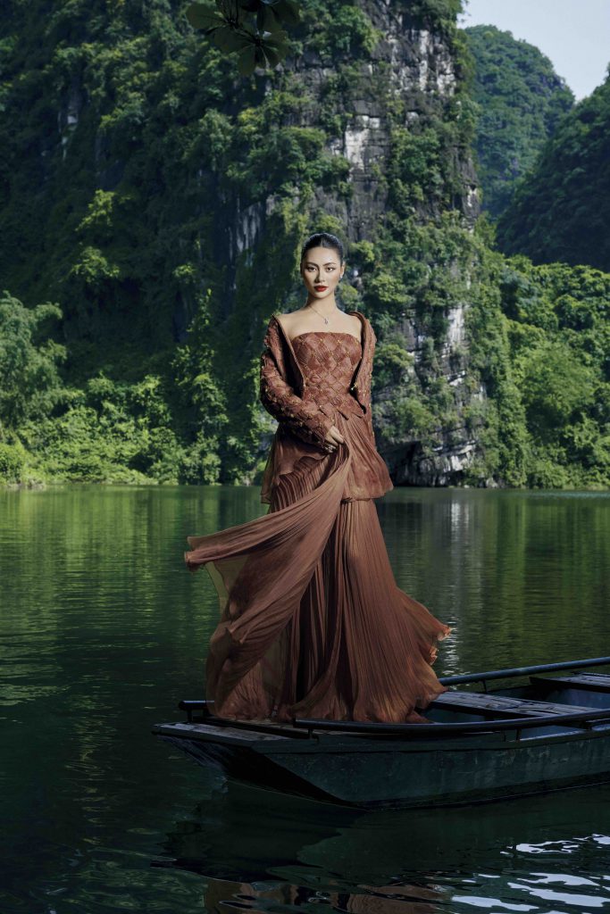 Người mẫu mặc váy lụa trên thuyền nhỏ giữa khung cảnh núi non hùng vĩ