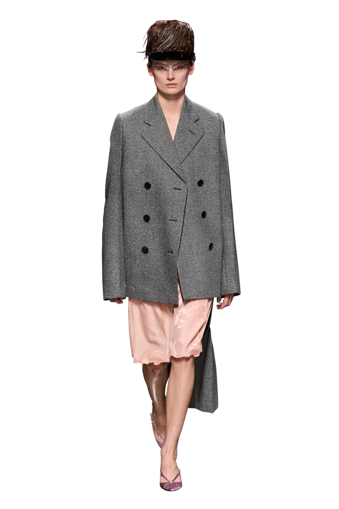 A model walks the runway wearing a gray tweed coat and pale pink slip dress