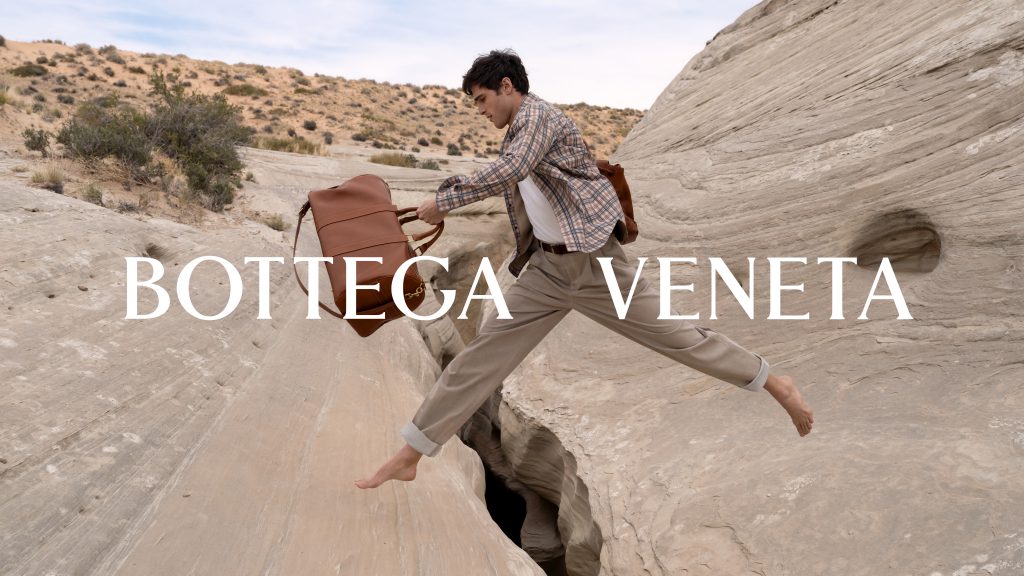 Người đàn ông nhảy qua khe núi đá mang túi xách Bottega Veneta