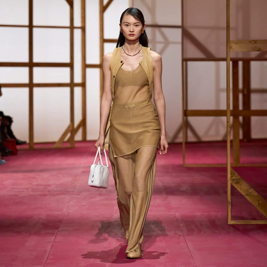 Người mẫu trình diễn trang phục màu be trên sàn diễn Hermès với chiếc túi xách trắng