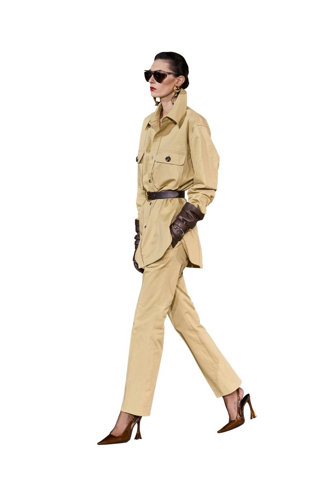 A model walks wearing a tan Saint Laurent suit and dark sunglasses
