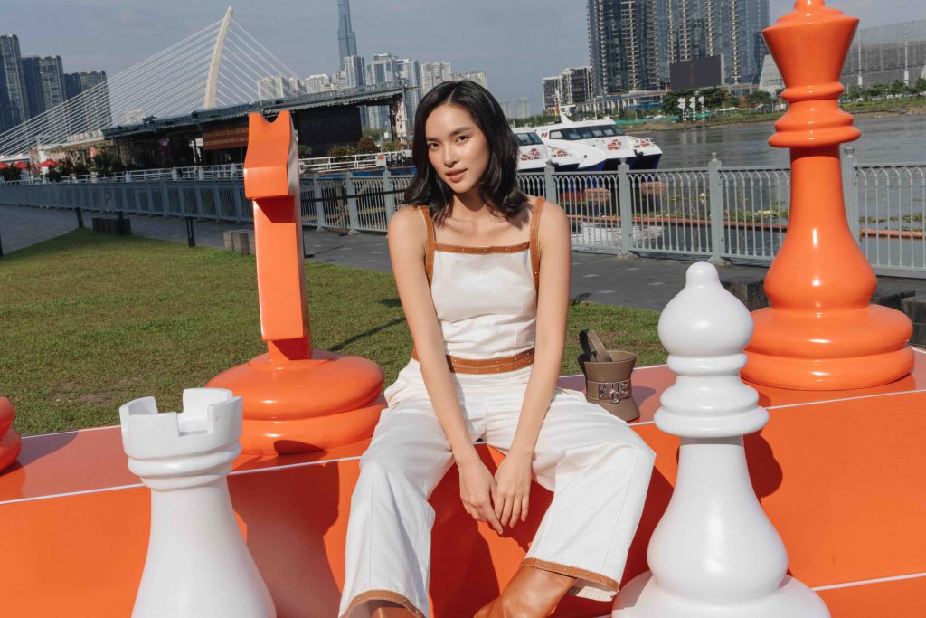 Cô gái ngồi trên quân cờ lớn trước khung cảnh thành phố Hồ Chí Minh hiện đại