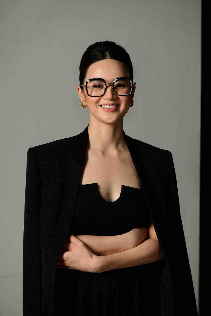 Chân dung người phụ nữ mặc áo blazer đen và đeo kính gọng vuông đang mỉm cười