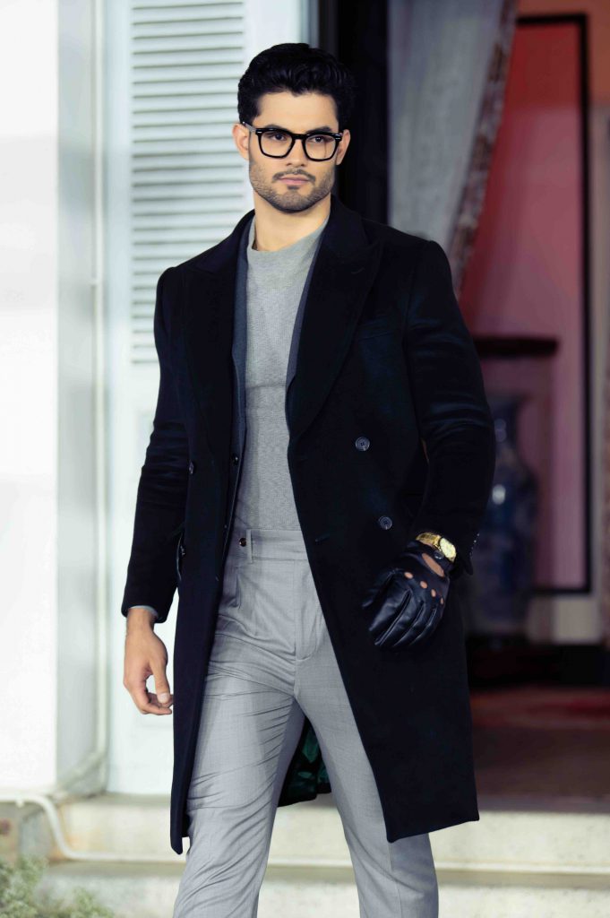 Một người đàn ông mặc áo khoác đen và quần tây sáng màu đang tạo dáng ngoài trời