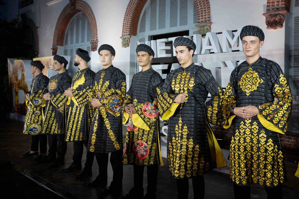 Nhóm người mẫu nam trình diễn áo dài lụa họa tiết rồng vàng trước kiến trúc Pháp cổ