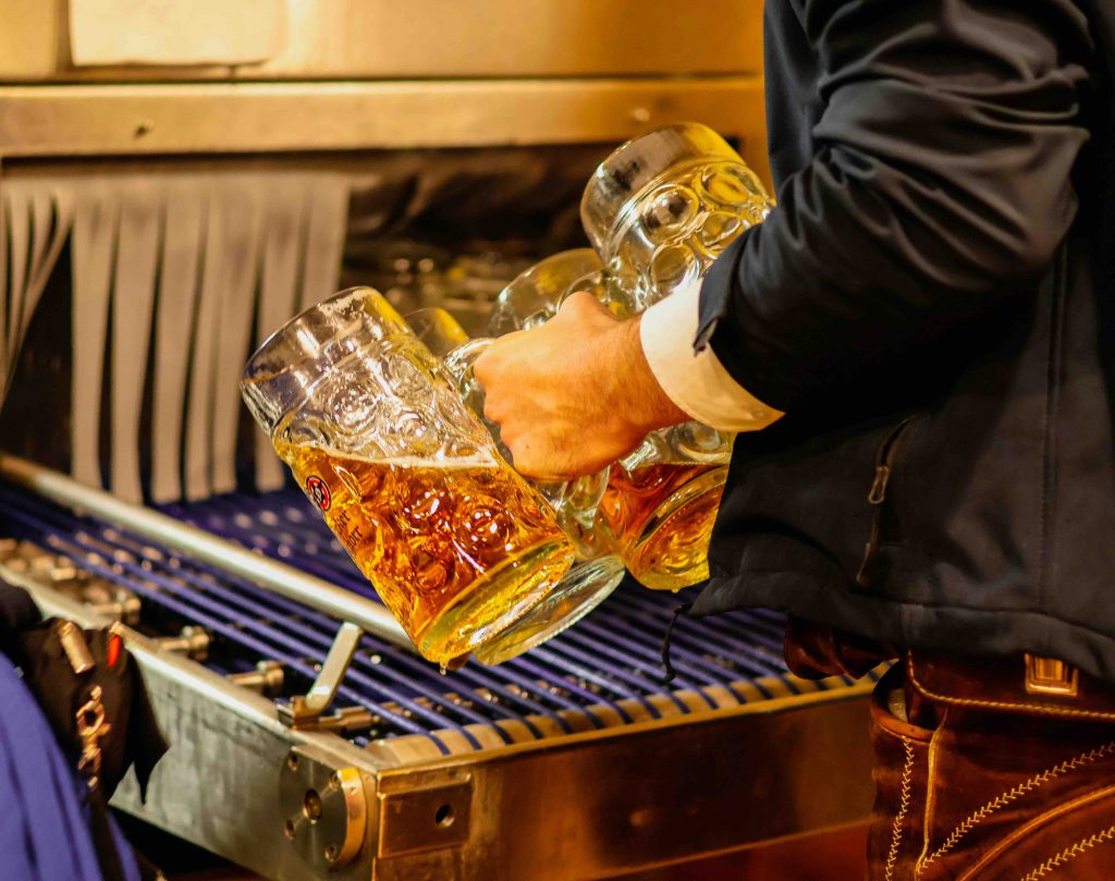 A person pours golden beer from a large mug into another mug