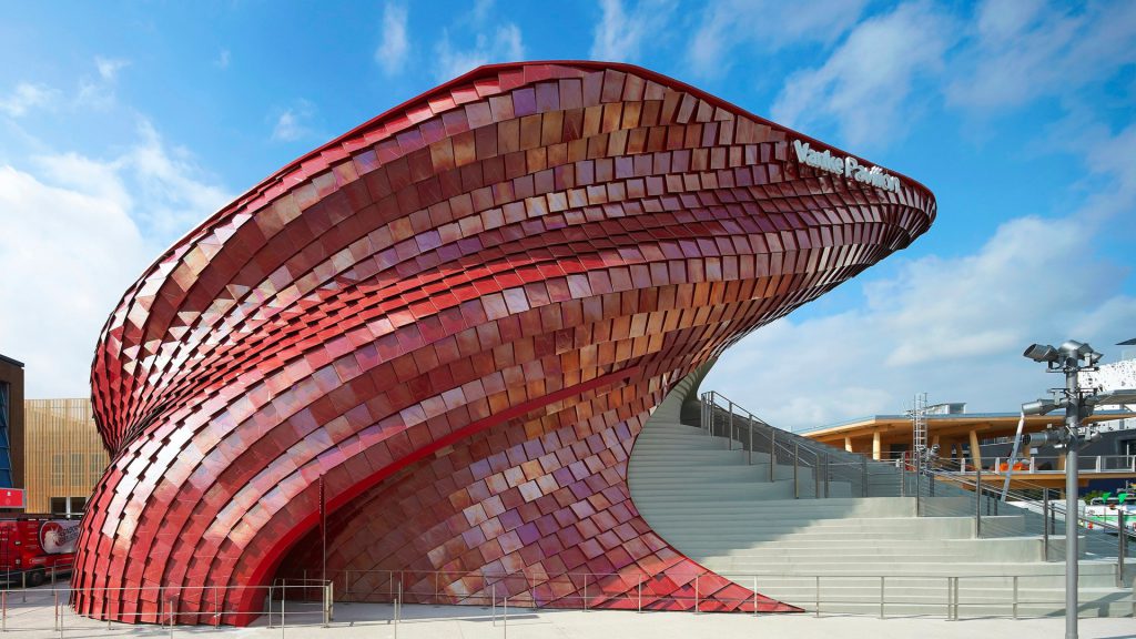 A red tiled building curves upward next to concrete steps under a blue sky