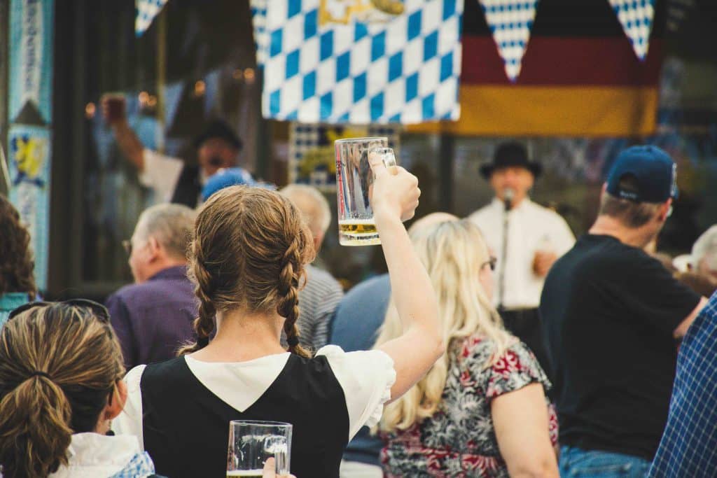 A woman raises a full beer mug at a lively outdoor festival with blue and white flags