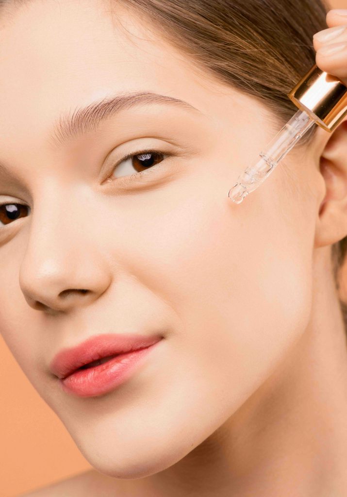 Cô gái xinh đẹp đang nhỏ serum lên má để dưỡng da