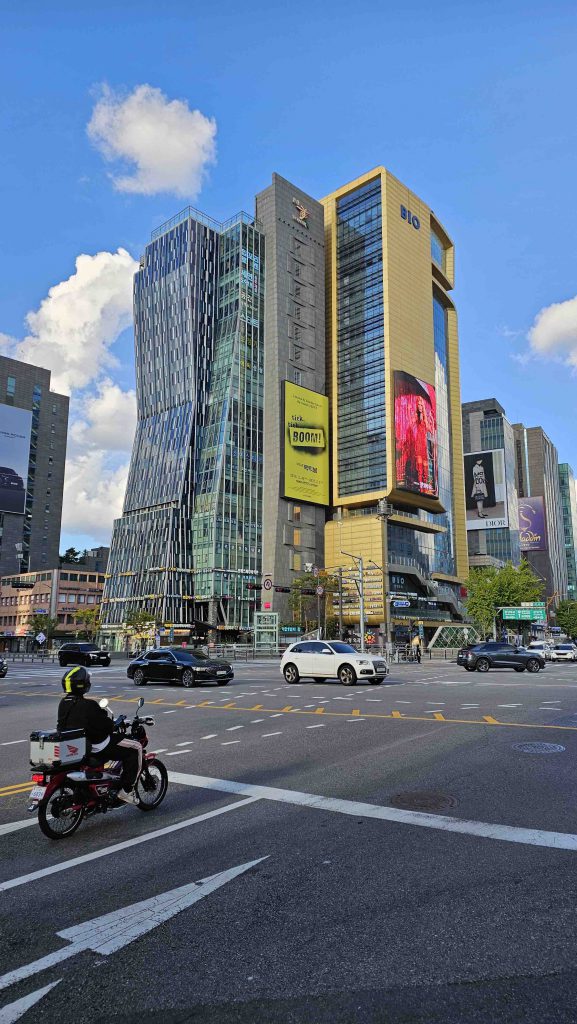 Toà nhà cao tầng với màn hình lớn ở Seoul có xe cộ và người đi xe máy bên dưới