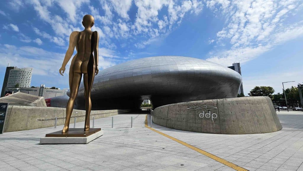 A golden statue stands before a modern building under a bright blue sky