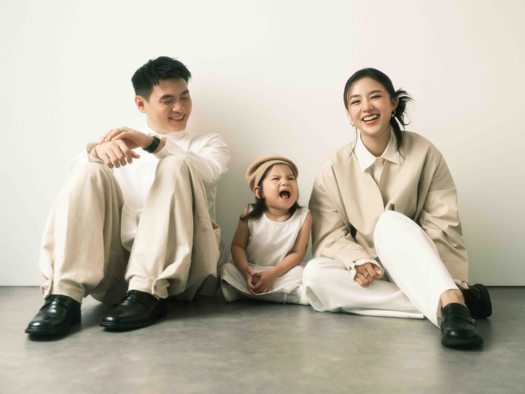 A happy family sits on the floor smiling at their laughing child