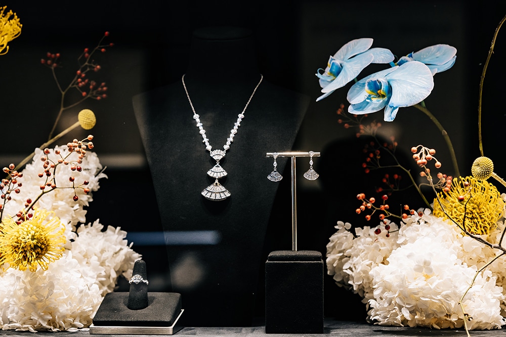 Dây chuyền và bông tai kim cương lấp lánh được trưng bày cùng hoa lan và hoa cúc