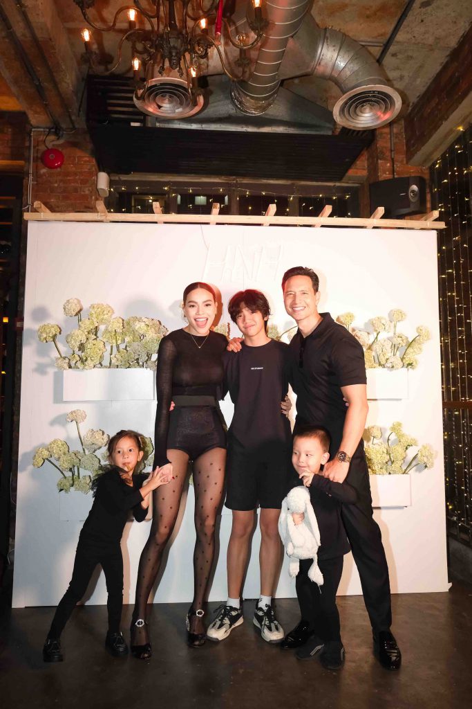 A family of five poses together smiling before a white floral backdrop