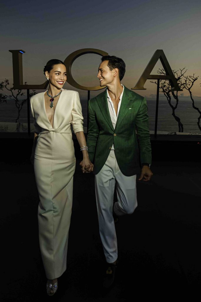 A couple holding hands walks toward the camera smiling with large letters behind them