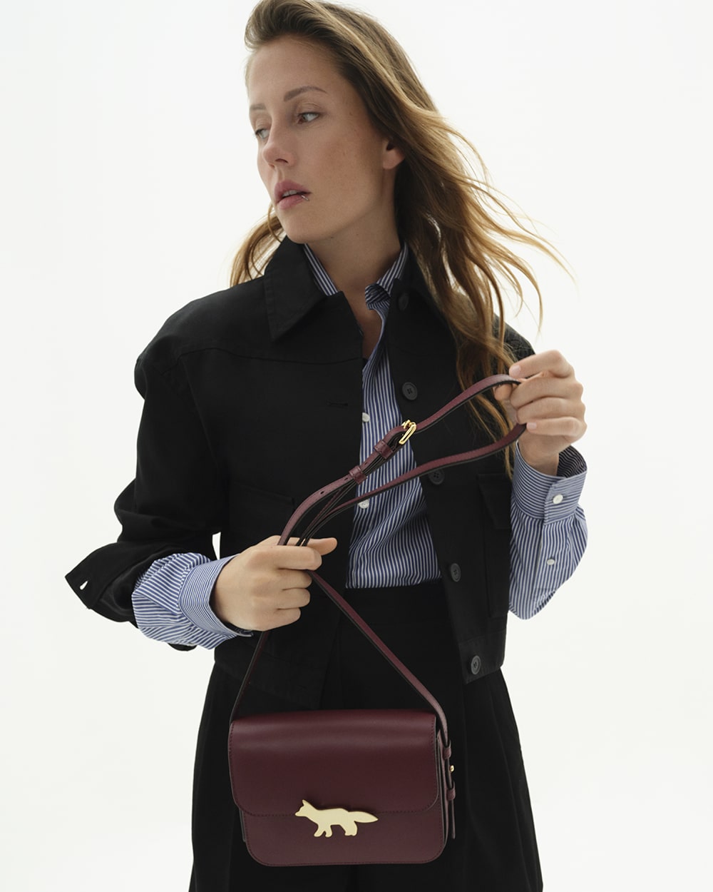 Người mẫu trẻ trung cầm túi xách da màu đỏ burgundy với biểu tượng con cáo bằng vàng