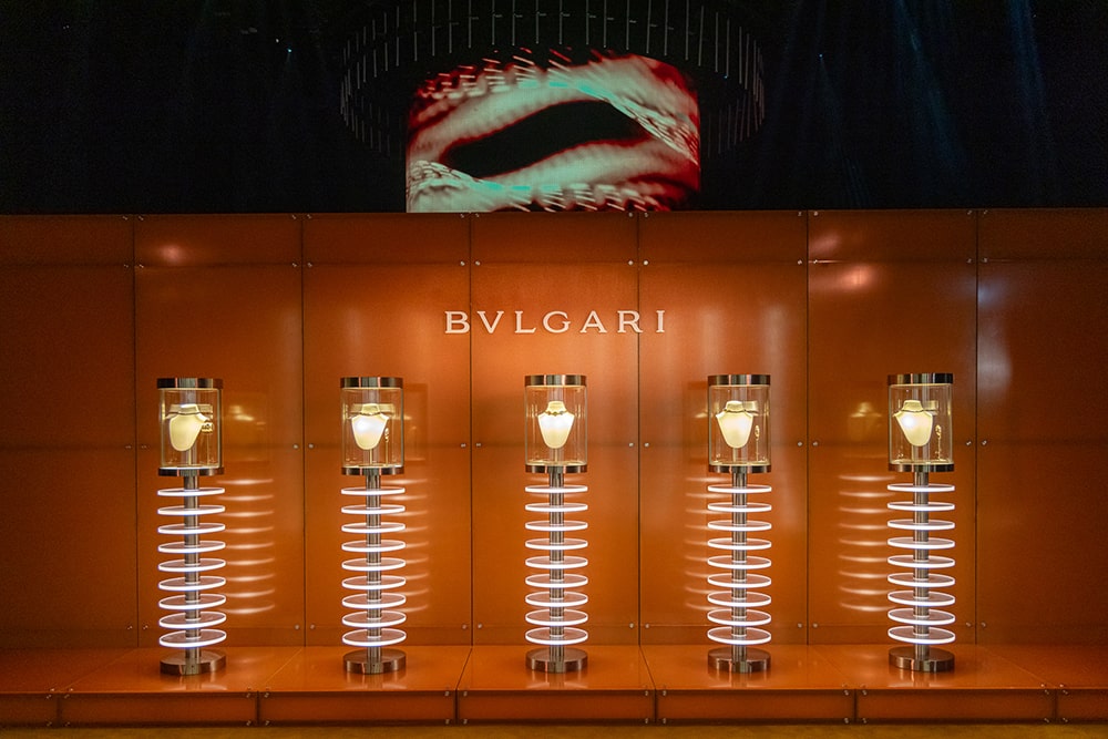 Trưng bày các mẫu trang sức Bvlgari Tubogas trên bục màu cam nổi bật với hình ảnh lớn phía sau