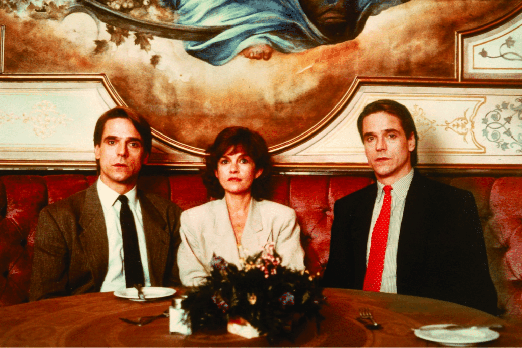 Ba nhân vật ngồi đối diện trong một nhà hàng sang trọng với tranh tường phía sau