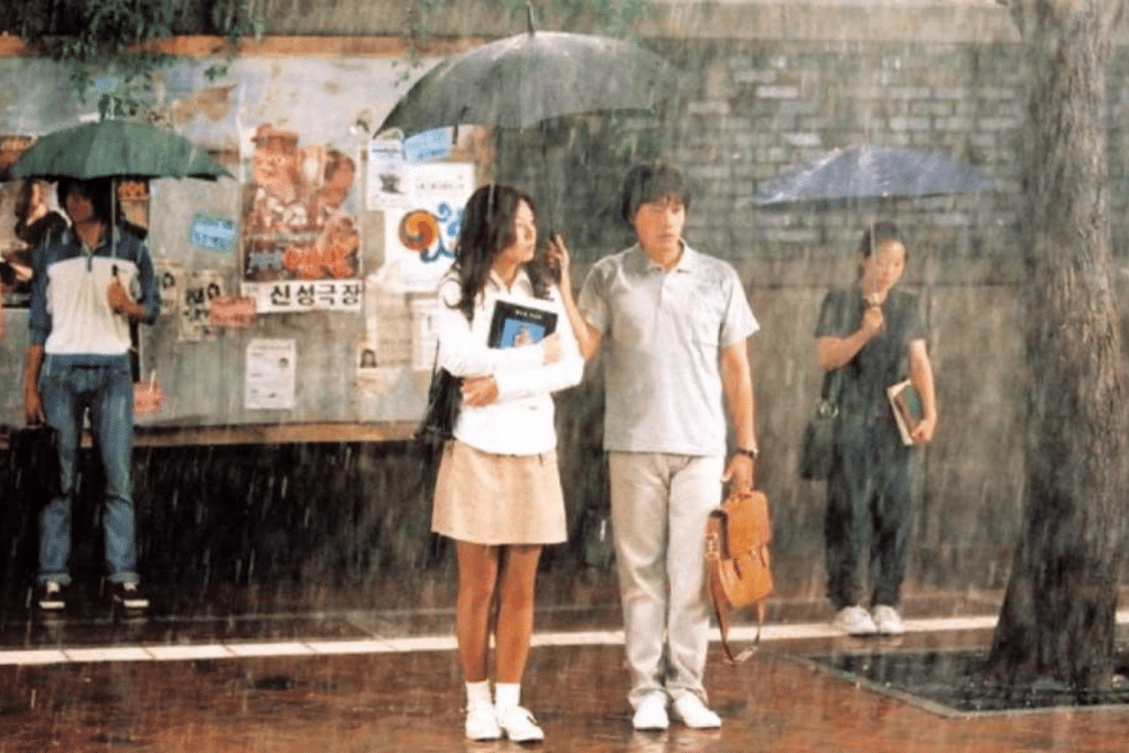 Cặp đôi trẻ đứng dưới mưa với ô đen cùng chiếc túi da màu cam