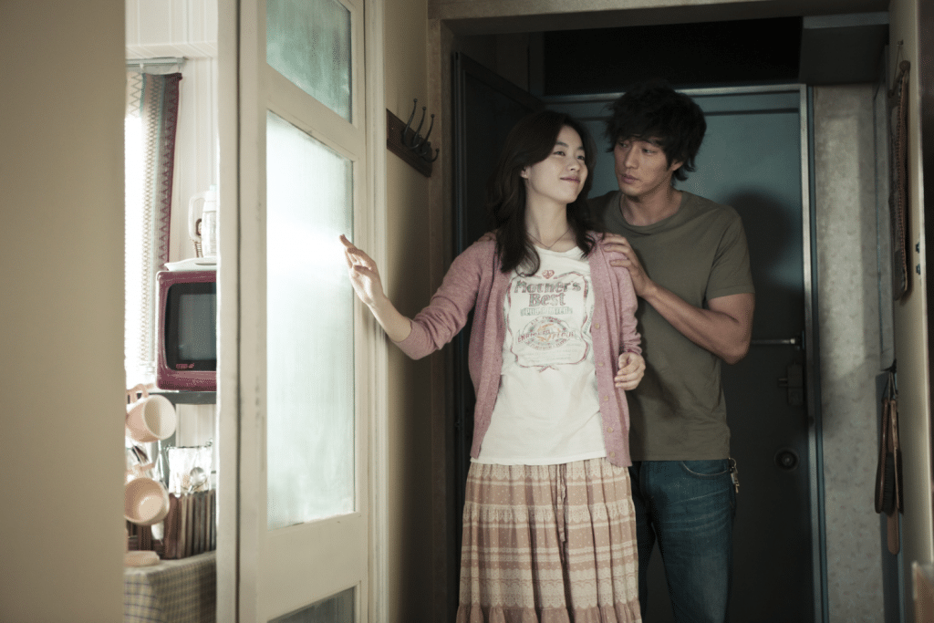 Cặp đôi trẻ đang đứng trước cửa nhà với ánh sáng dịu nhẹ và biểu cảm tình cảm