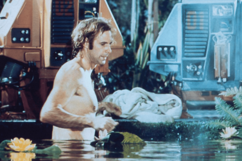 Người đàn ông cởi trần đang lau người gần một hồ nước với hoa súng