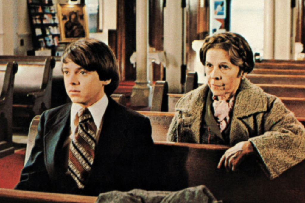 Cậu bé và người phụ nữ lớn tuổi ngồi trên ghế dài trong nhà thờ nhìn về phía trước