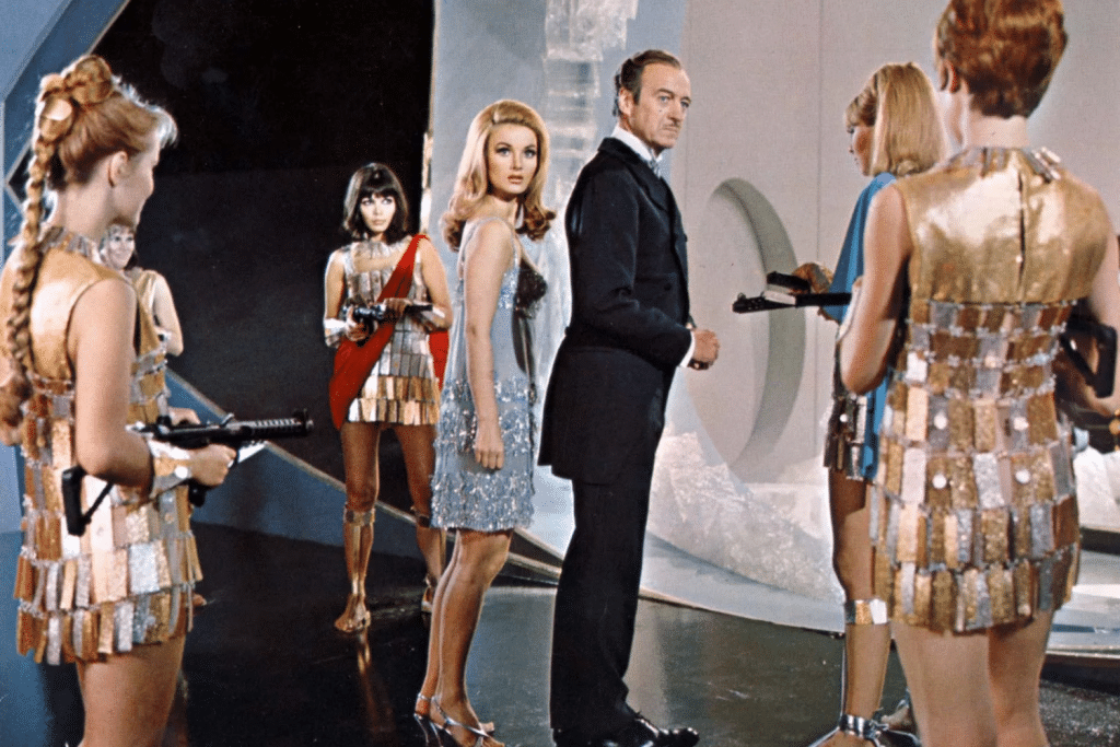 Người đàn ông lịch lãm đứng giữa các cô gái mặc trang phục lấp lánh cầm súng