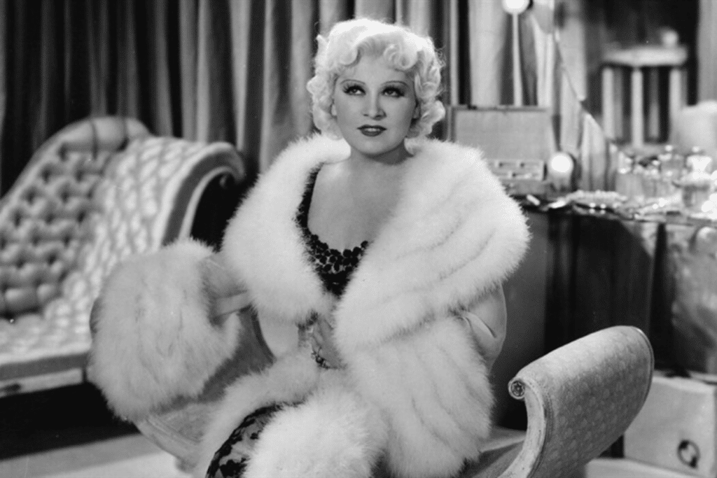 Nữ diễn viên tóc bạch kim quyến rũ ngồi trên ghế bọc vải với áo choàng lông trắng