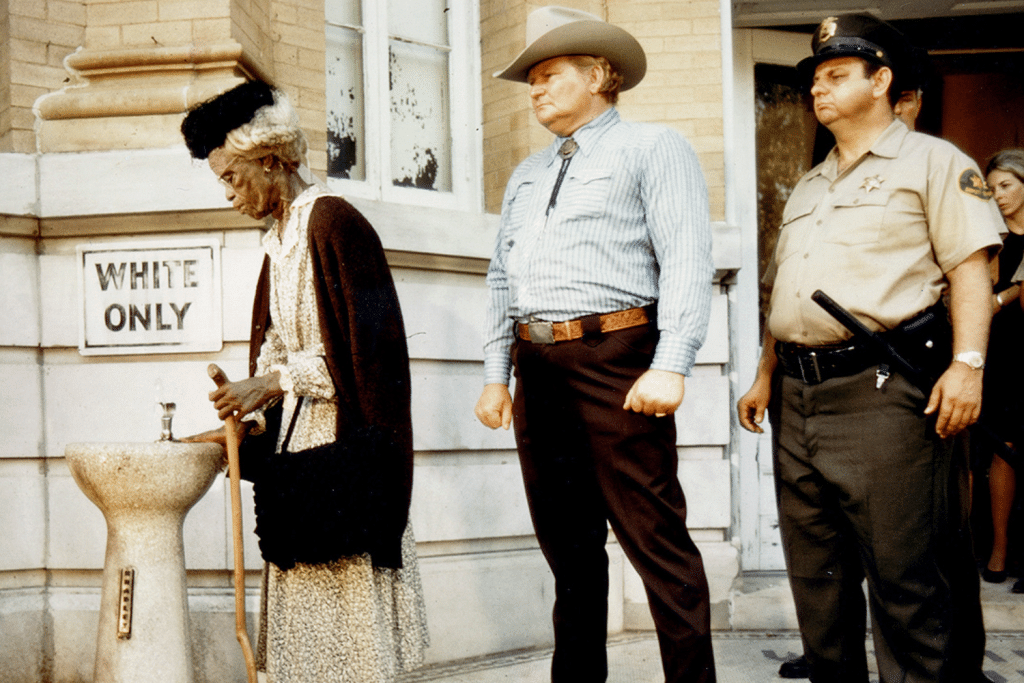 Một cụ bà da màu uống nước tại vòi nước công cộng có biển "Chỉ dành cho người da trắng"