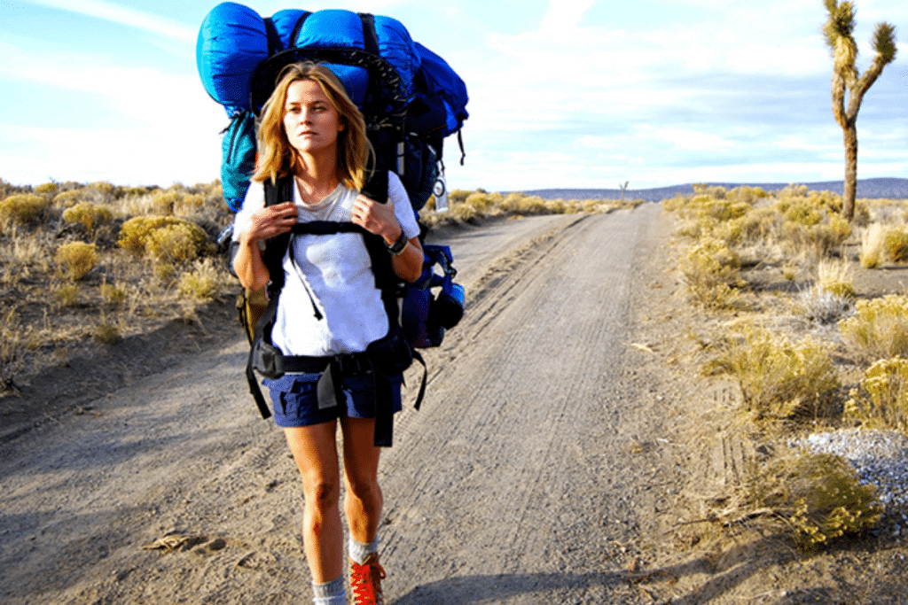 Cô gái trẻ mang balo lớn đi bộ trên con đường đất giữa sa mạc khô cằn