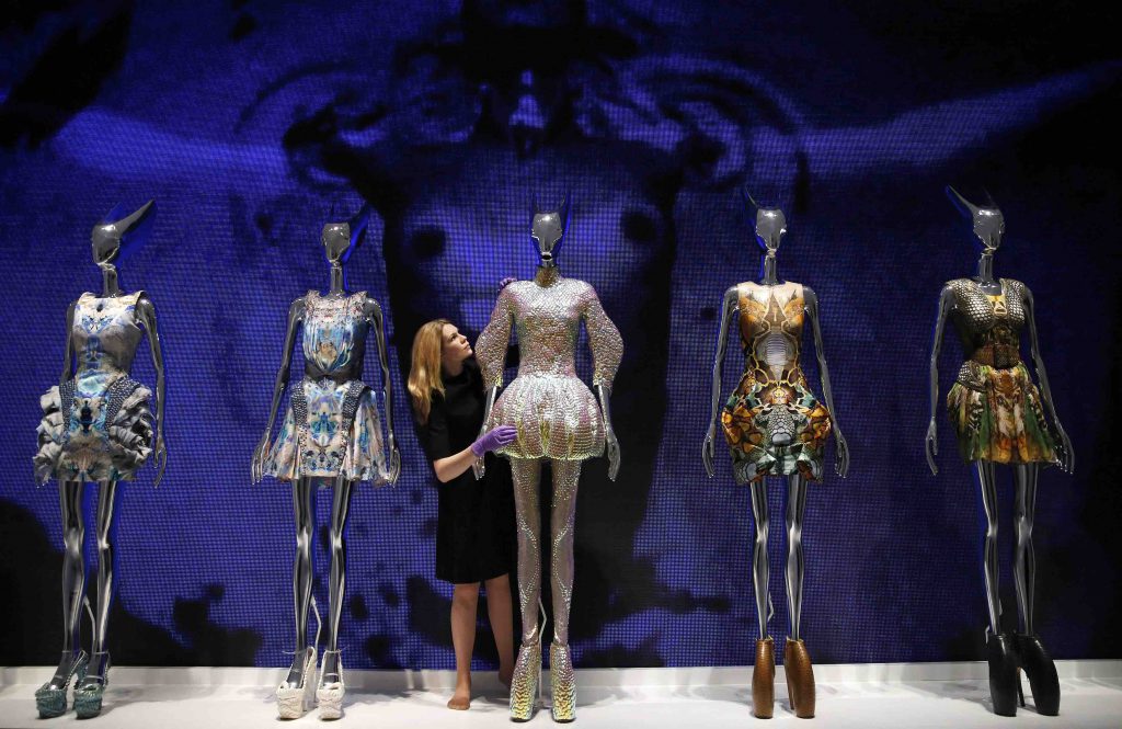 A woman adjusts avant-garde designs displayed on metallic mannequins before a large blue face