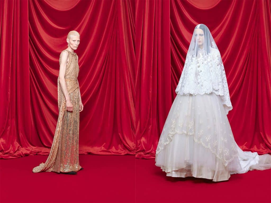 Two models stand before red curtains wearing elegant gowns one gold one white