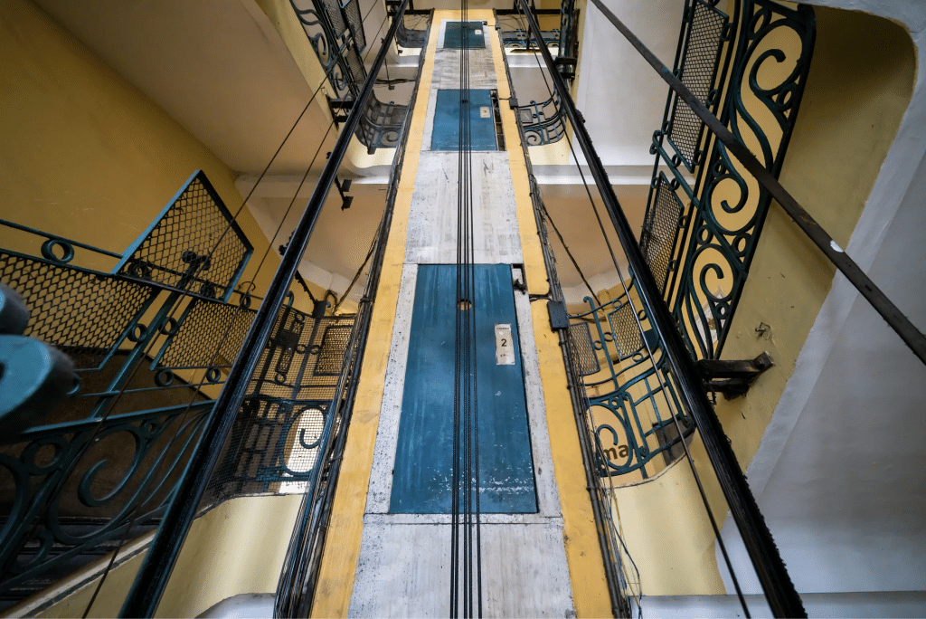 A vintage elevator rises within a yellow and black metalwork shaft
