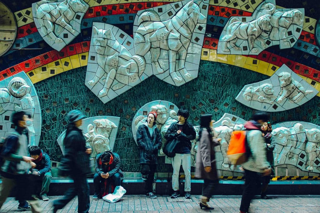 Người dân Tokyo đứng và ngồi trước bức tường gạch mosaic hình ảnh các loài động vật