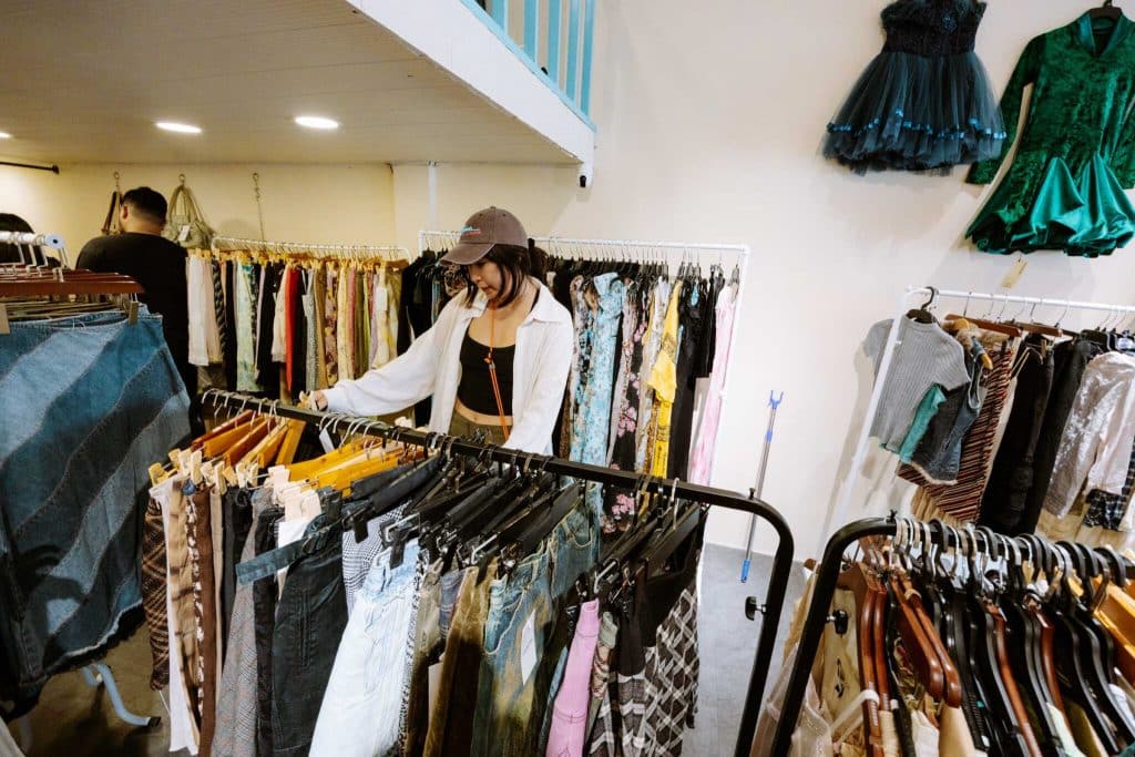 A woman browses racks of colorful clothes inside a bustling vintage shop