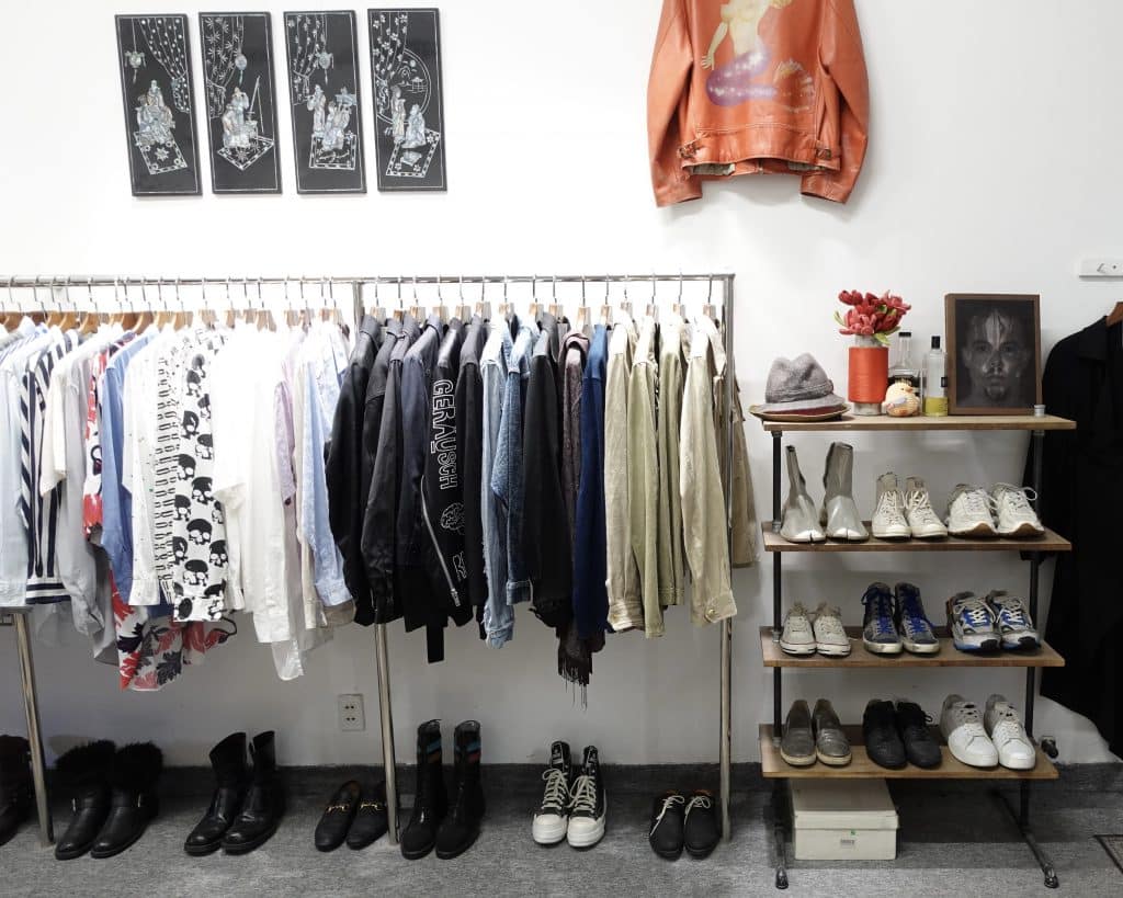 Clothing racks display shirts jeans and jackets near shoes and wall art