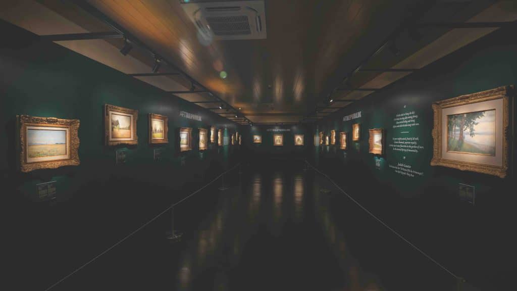 A long gallery displays many framed paintings along dark green walls